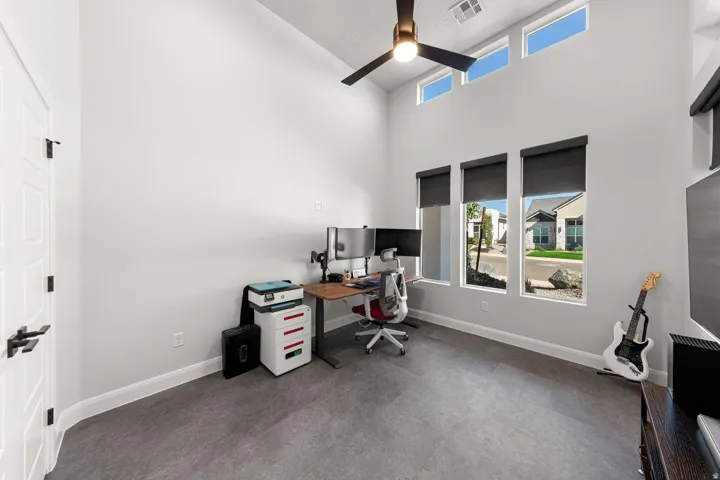Vaulted ceiling with a ceiling fan, transom windows, three vertical windows with roller shades, and dark wood-finish flooring