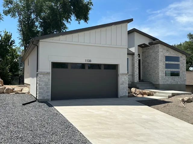 Contemporary architectural design featuring a multi-textured facade, an integrated garage with transom windows, a concrete driveway, and an entryway with stone cladding