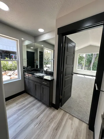 Wood-finish flooring, dark wood vanity with stone countertop, integrated sink, and recessed lighting