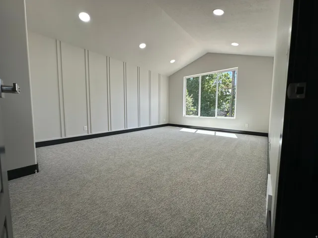 Vaulted ceiling room featuring recessed lighting, a large picture window, textured wall paneling, and dark trim