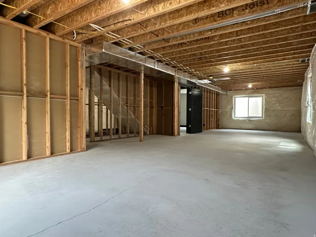 Unfinished basement with exposed ceiling joists, concrete flooring, framed wall sections, and a window for natural illumination