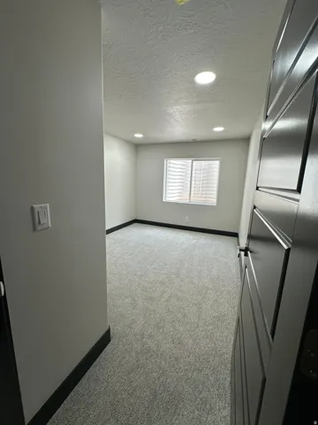 Recessed lighting, light gray carpet, window with blinds, dark trim, and a paneled interior door