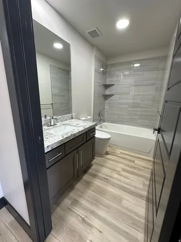 Bathroom featuring a vanity with a white countertop and undermount sink, wood-finish flooring, a tiled shower/tub combination, and recessed lighting