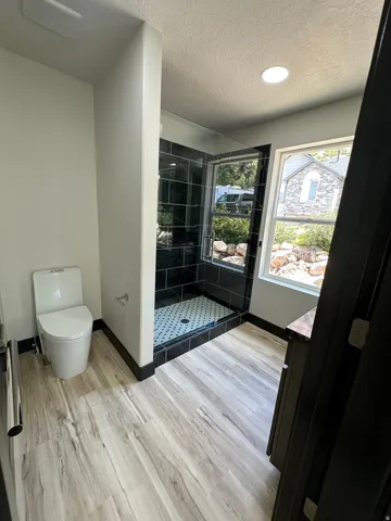Wood-finish flooring, dark wood-finish vanity with stone countertop, walk-in shower with glass enclosure, black tile walls, and white and black patterned floor