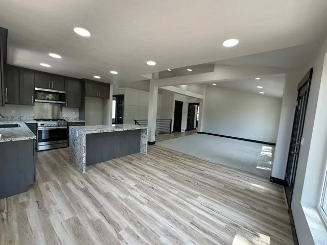 Spacious kitchen with wood-finish flooring, stone countertops, stainless steel appliances, and recessed lighting