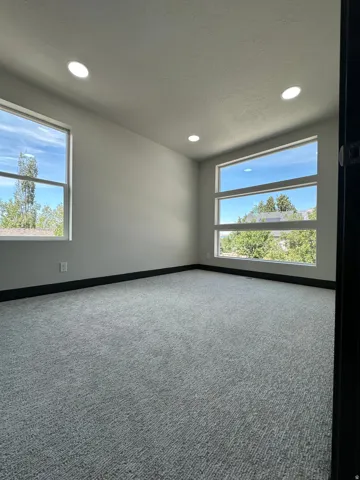 Recessed lighting, light gray walls, textured gray carpeting, two large windows, and a three-panel horizontal window