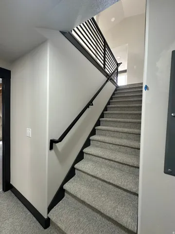 Carpeted staircase featuring a black metal railing and a black handrail