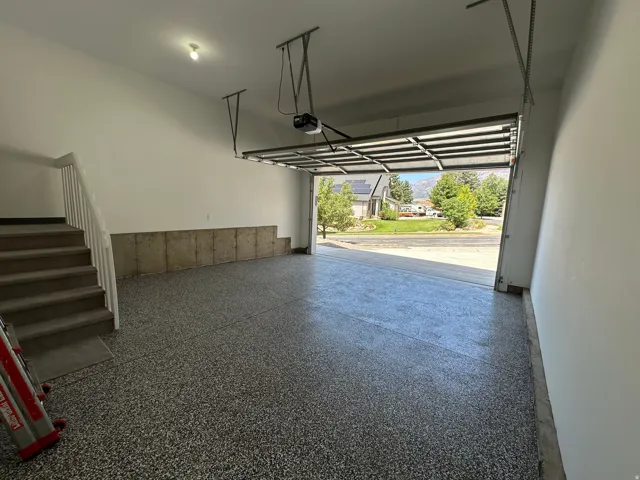 Spacious garage featuring epoxy flooring, an automatic garage door opener, and interior stairs with a white railing