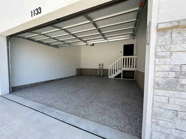 Spacious garage featuring an epoxy-coated floor, white interior walls, and a white-painted staircase with railing