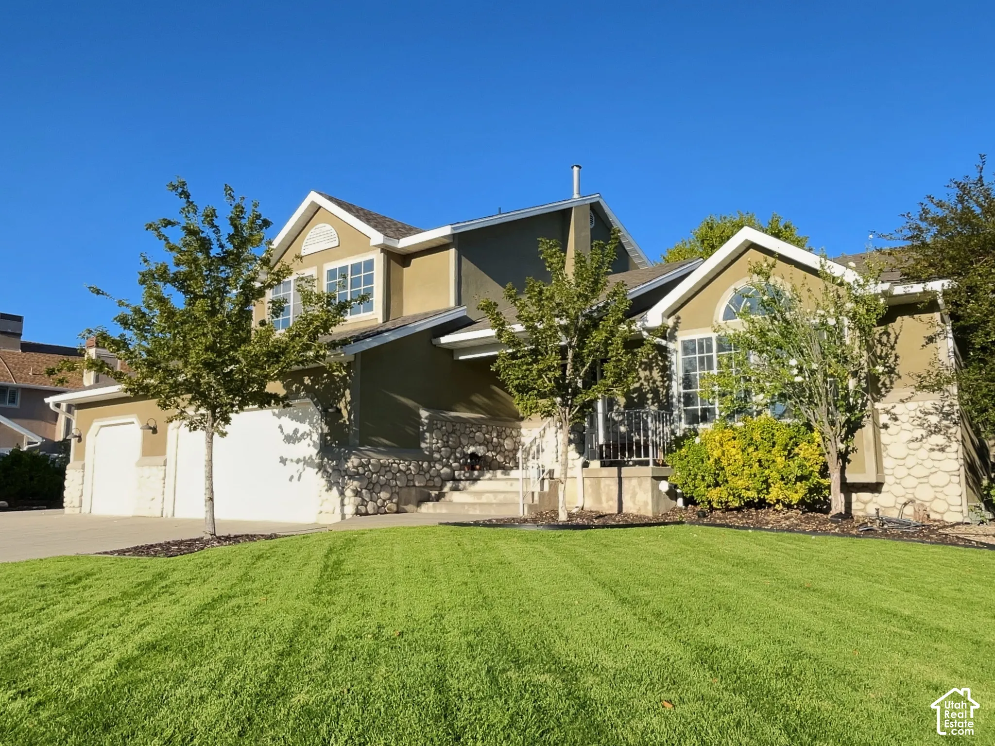 Stucco exterior with stone accents, arched window, attached two-car garage, and a manicured lawn