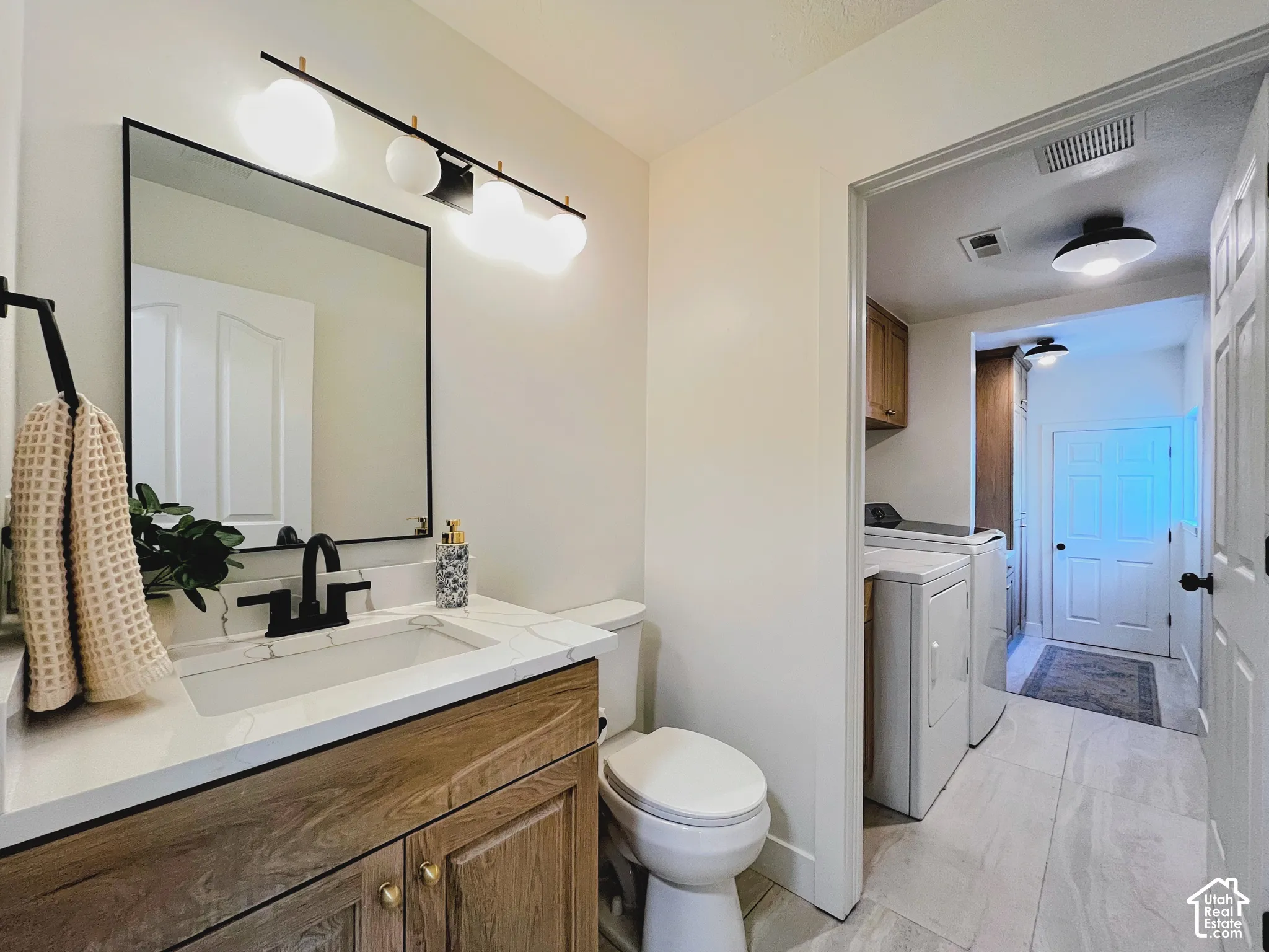 Vanity with wood-finish cabinetry, quartz countertop, and black fixtures