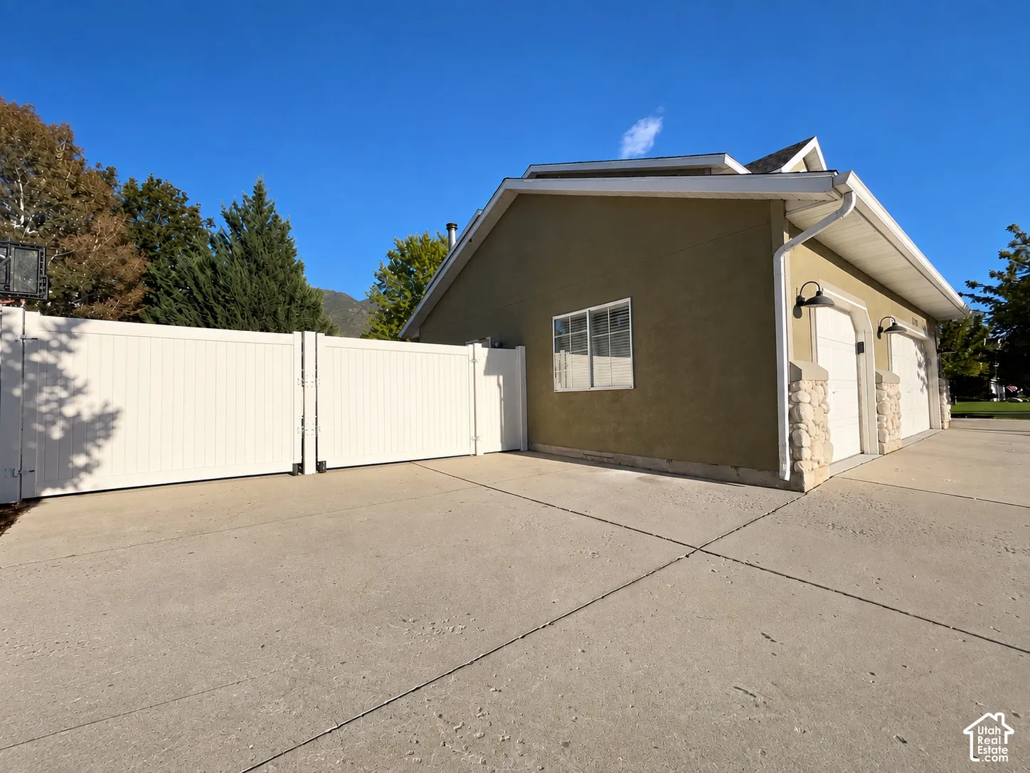 Two-car garage with carriage-style doors, stone column accents, exterior wall sconces, and a stucco finish