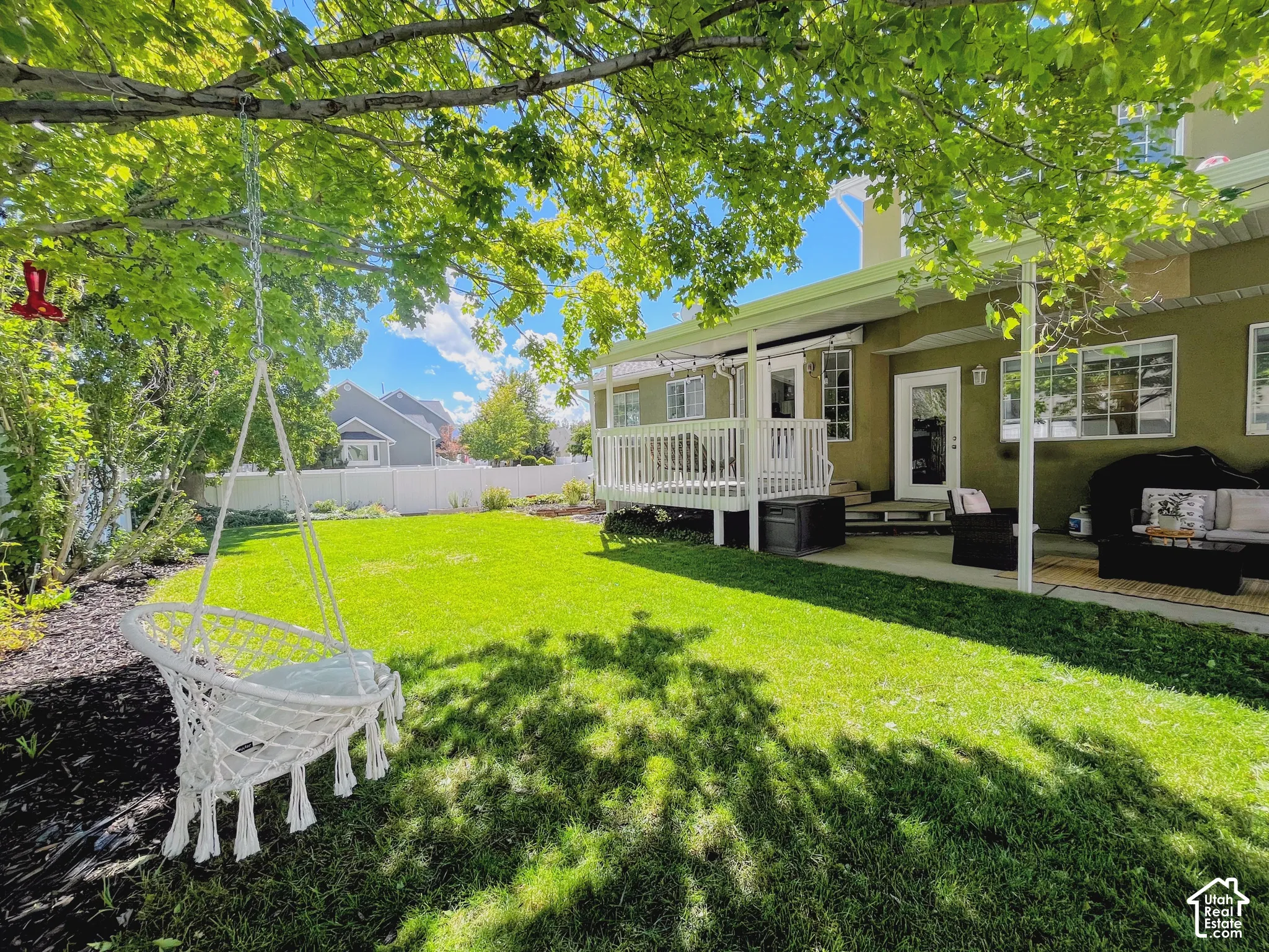 Expansive green lawn with a white privacy fence, mature trees, and a ground-level patio