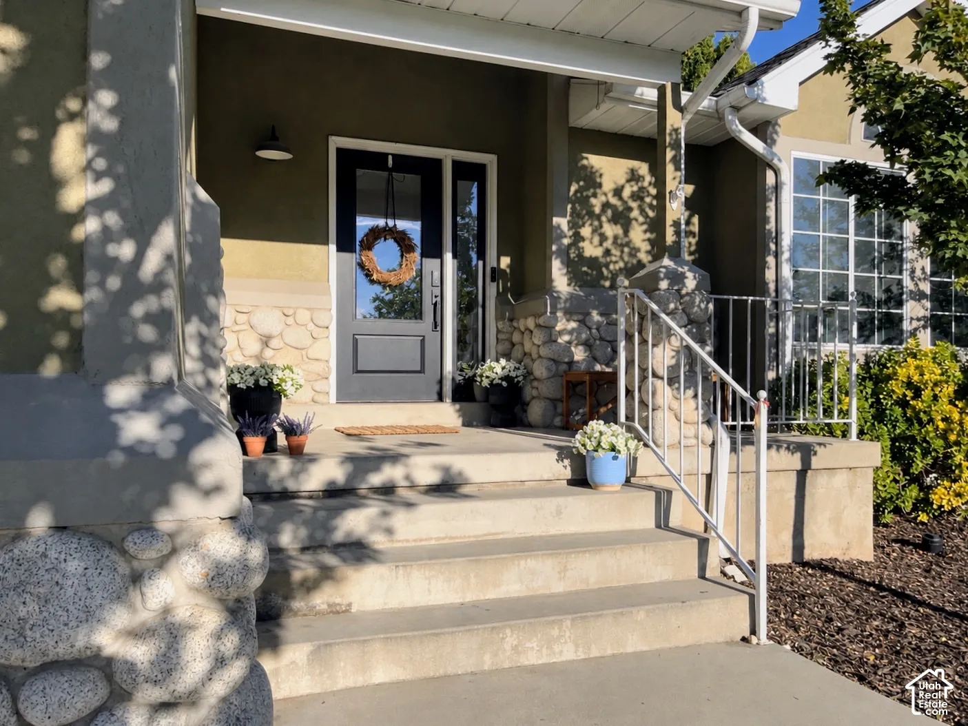 Entryway featuring a dark-paneled door with glass inserts, stone-clad columns, stucco exterior, multi-pane windows, and concrete steps with a metal handrail