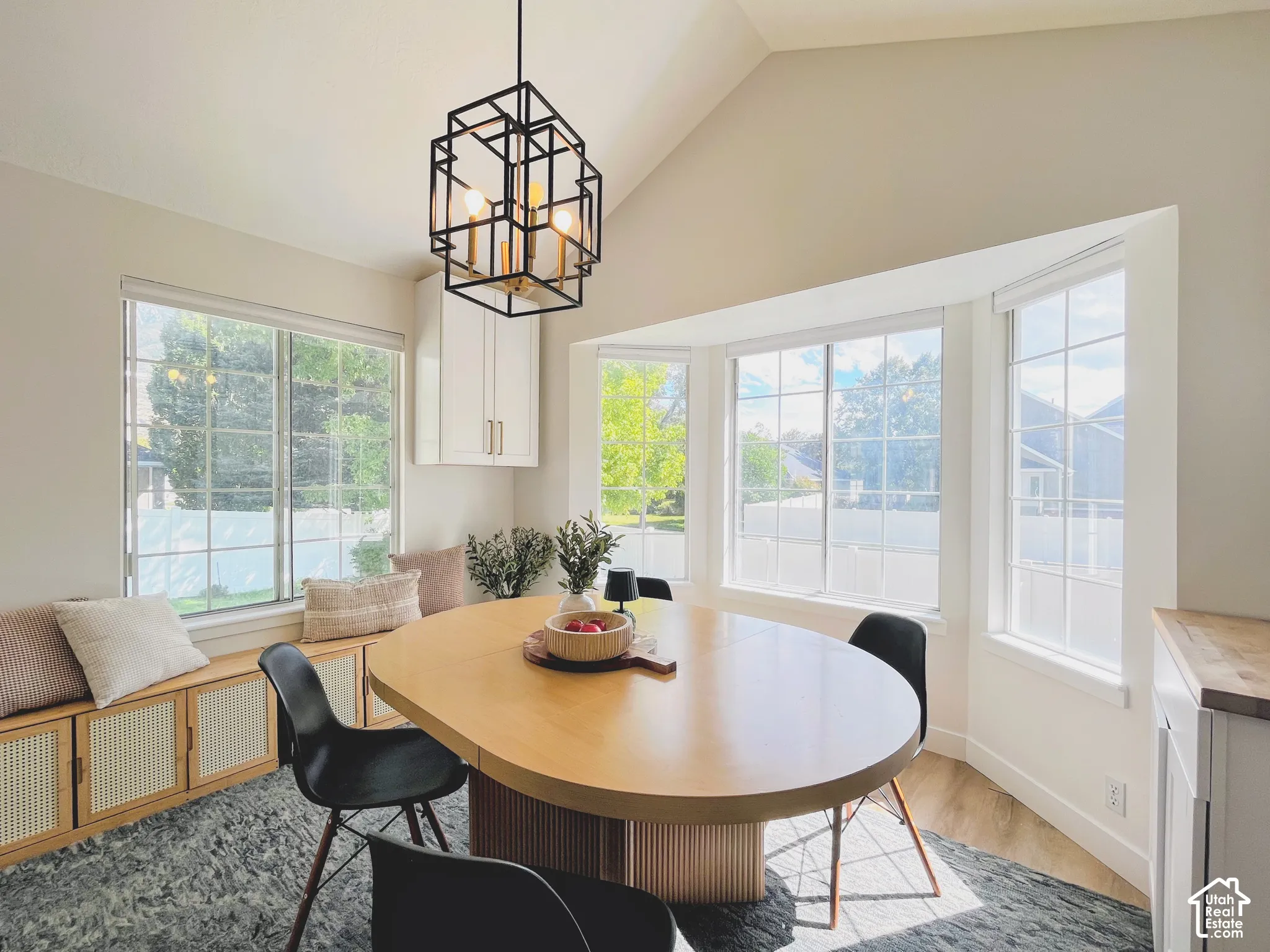 Vaulted ceiling with a geometric pendant light fixture, bay windows, wood-finish flooring, and built-in cabinetry