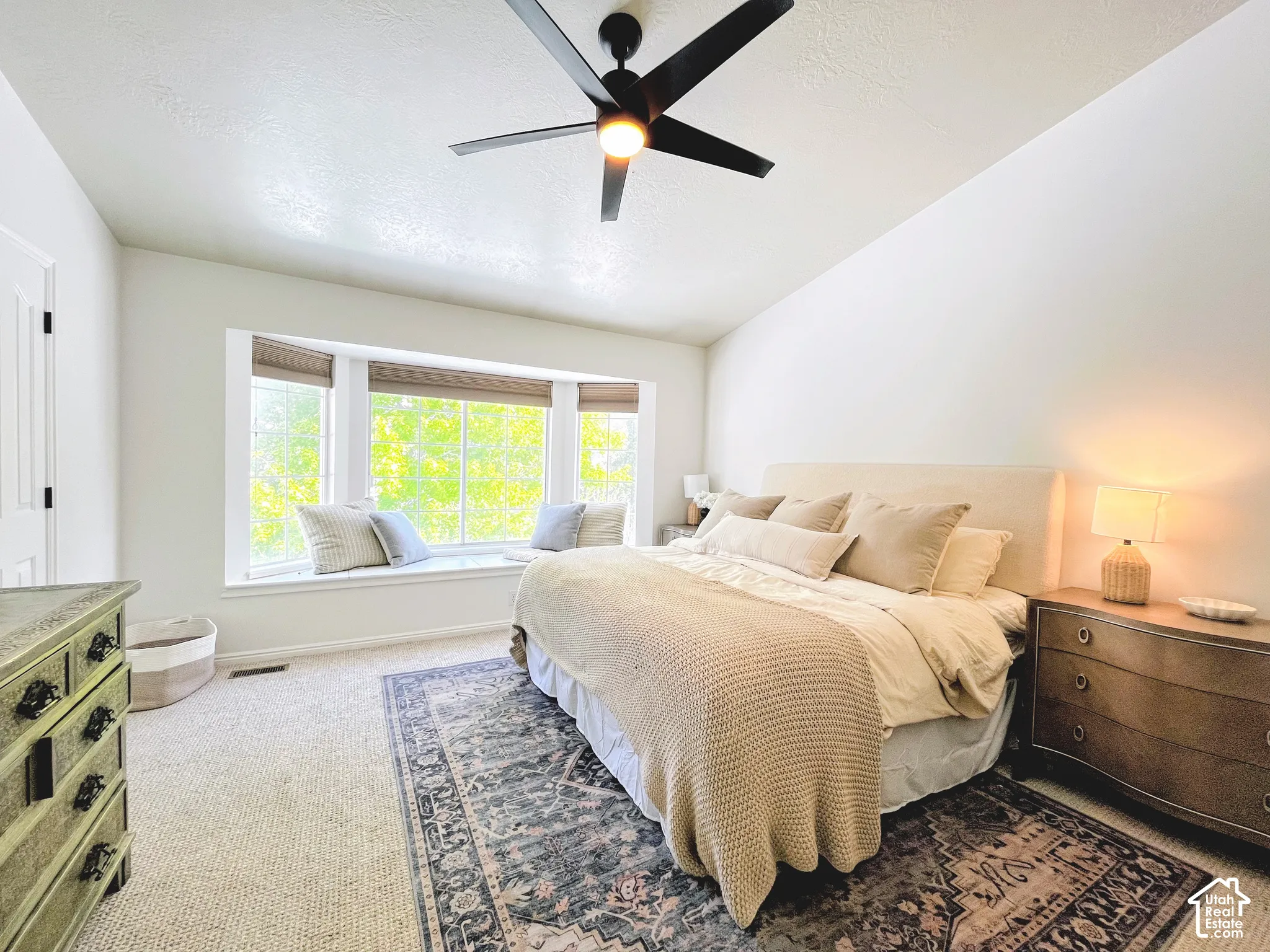 Carpet flooring, bay window with window seat, ceiling fan, and white walls