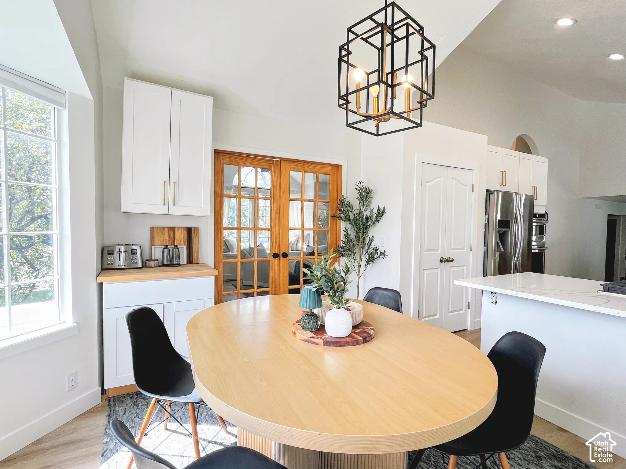 Vaulted ceiling, white cabinetry with gold-tone hardware, wood-finish flooring, French doors, and a kitchen island with a light-tone countertop