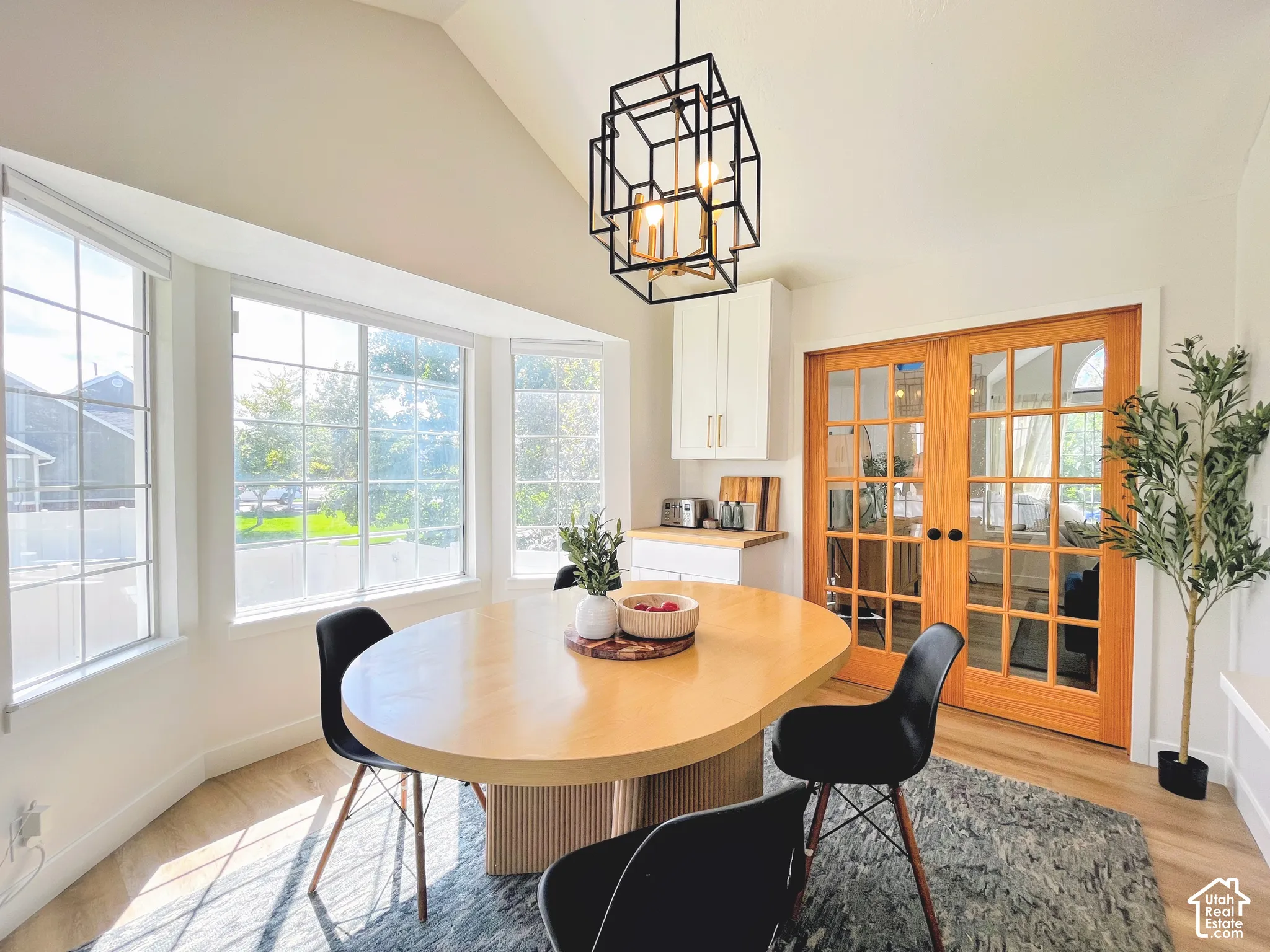 Vaulted ceiling, geometric pendant light fixture, bay window with multiple panes, wood-finish flooring, and double French doors