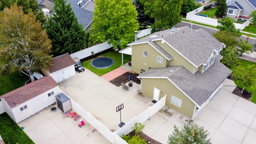 Expansive concrete driveway, two detached storage sheds, fenced backyard with a lawn area, and mature trees providing shade