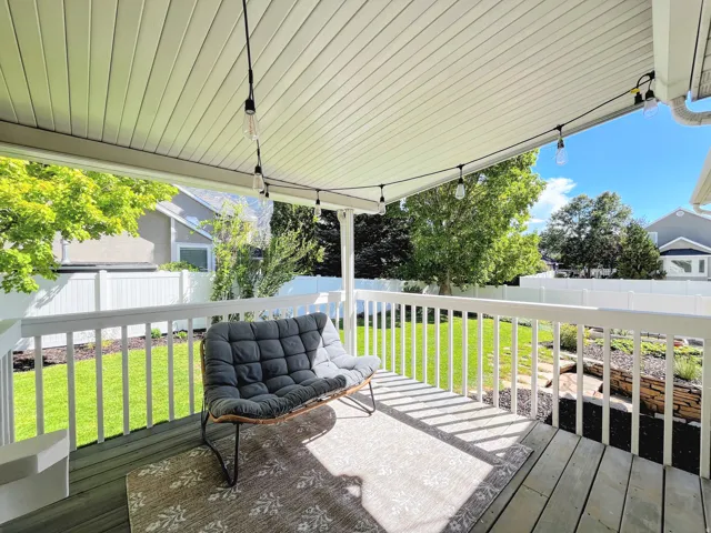 Covered deck with a slatted ceiling, string lighting, and white railings