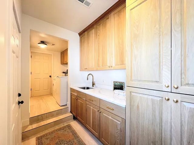 Light wood-finish cabinetry, white countertop, and integrated sink with a gooseneck faucet