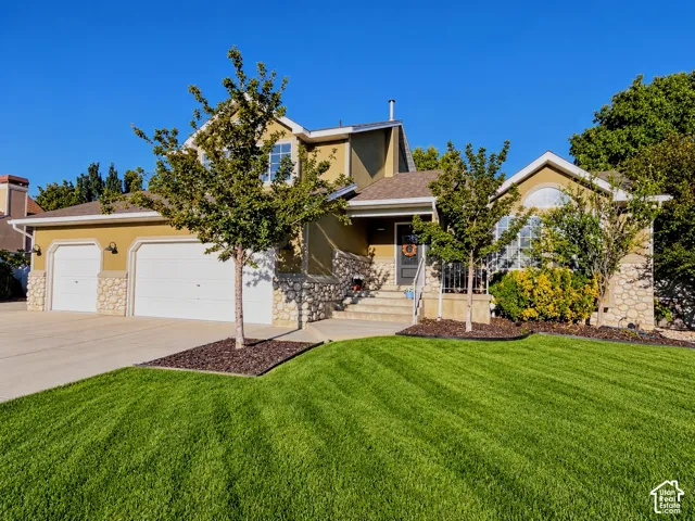 Stucco exterior with stone accents, two-car garage, arched entry, mature landscaping, and a manicured lawn