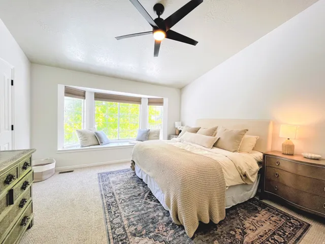 Carpet flooring, bay window with window seat, ceiling fan, and white walls