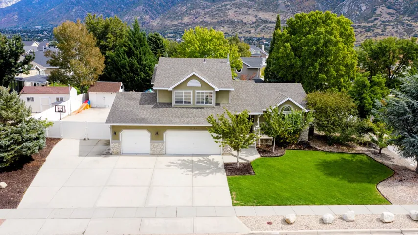 Expansive driveway, two-car garage, mature trees, manicured lawn, and mountain backdrop