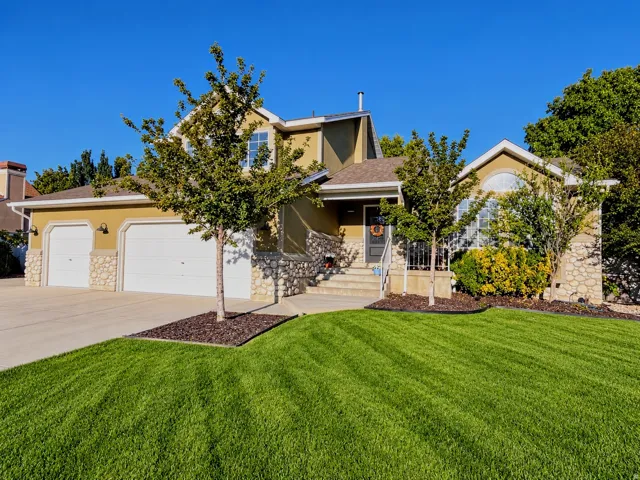 Stucco exterior with stone accents, two-car garage, arched entry, mature landscaping, and a manicured lawn