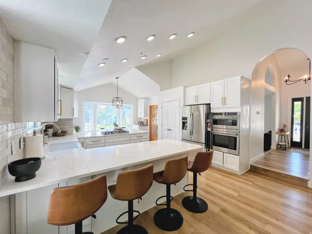 Kitchen featuring white cabinetry, quartz countertops, stainless steel appliances, wood-finish flooring, and vaulted ceilings