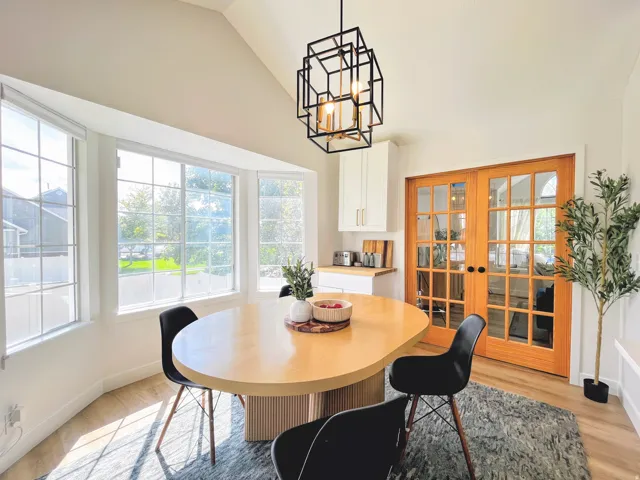 Vaulted ceiling, geometric pendant light fixture, bay window with multiple panes, wood-finish flooring, and double French doors
