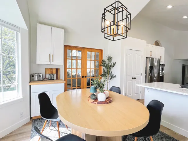Vaulted ceiling, white cabinetry with gold-tone hardware, wood-finish flooring, French doors, and a kitchen island with a light-tone countertop