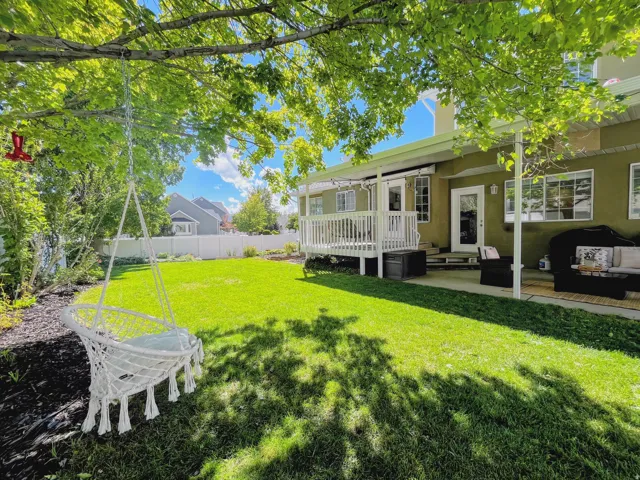 Expansive green lawn with a white privacy fence, mature trees, and a ground-level patio