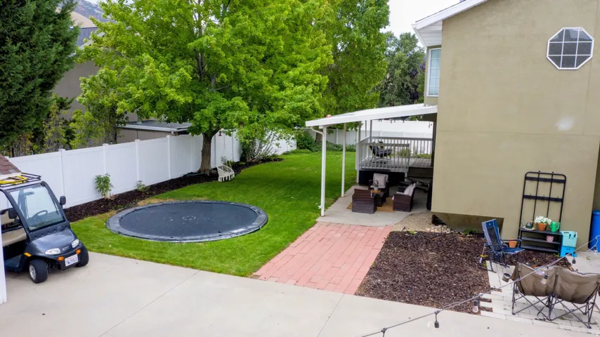 Expansive green lawn, white privacy fencing, mature trees, multi-level deck with covered patio, and brick paver pathway