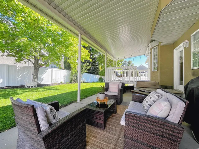 Covered patio with concrete flooring, private backyard with mature trees, and white privacy fencing