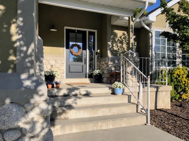 Entryway featuring a dark-paneled door with glass inserts, stone-clad columns, stucco exterior, multi-pane windows, and concrete steps with a metal handrail