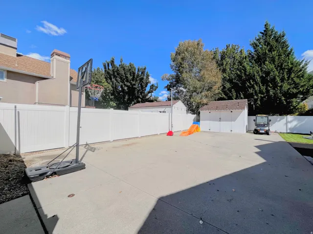 Expansive concrete patio with white privacy fencing, two storage sheds, and mature perimeter trees