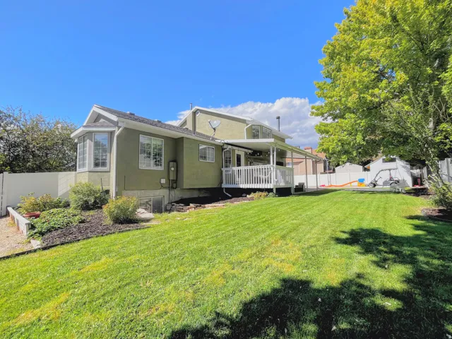 Expansive green lawn, a covered white deck, exterior bay window, stucco exterior, and mature landscaping