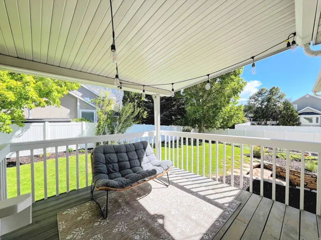 Covered patio with wood-finish decking, white railings, and string lighting