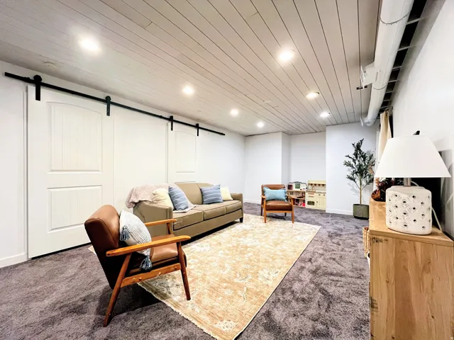 Recessed lighting, planked ceiling, white walls, and a barn door system with black hardware