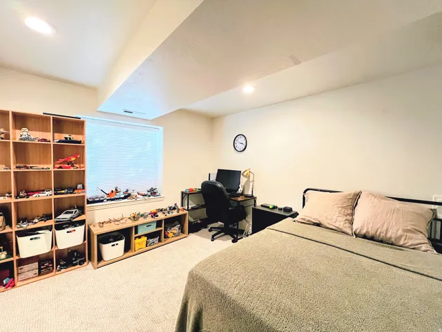 Recessed ceiling lighting, a window with horizontal blinds, built-in shelving, carpet flooring, and a black metal bed frame