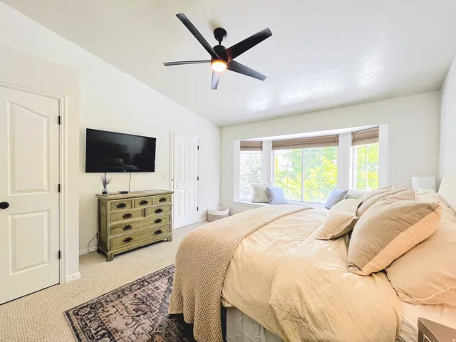Recessed bay window with integrated bench seating, modern ceiling fan with lighting, wall-mounted television, and neutral carpet flooring