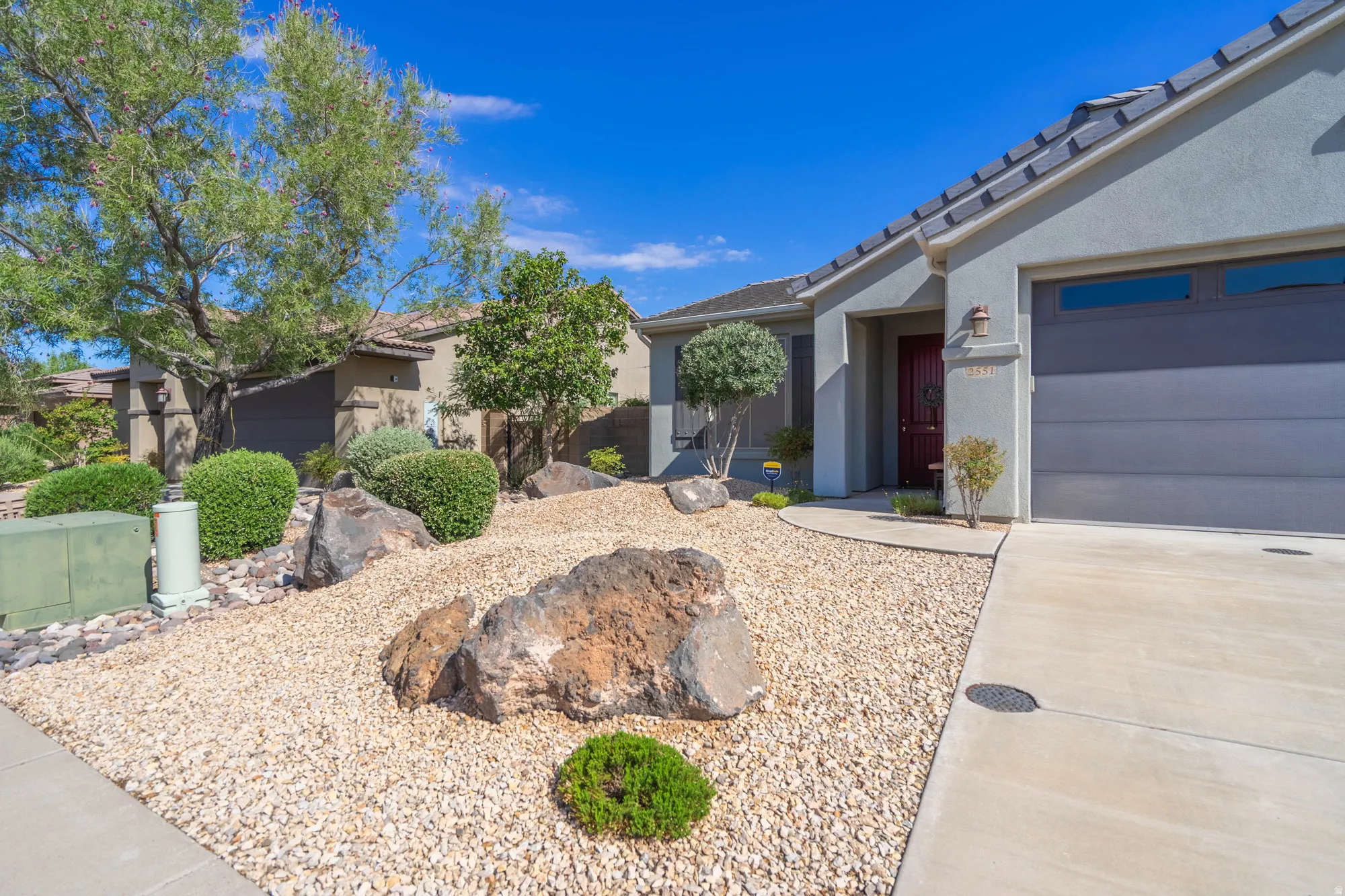 Stucco exterior with a dark tile roof, a grey garage door, and a red entry door