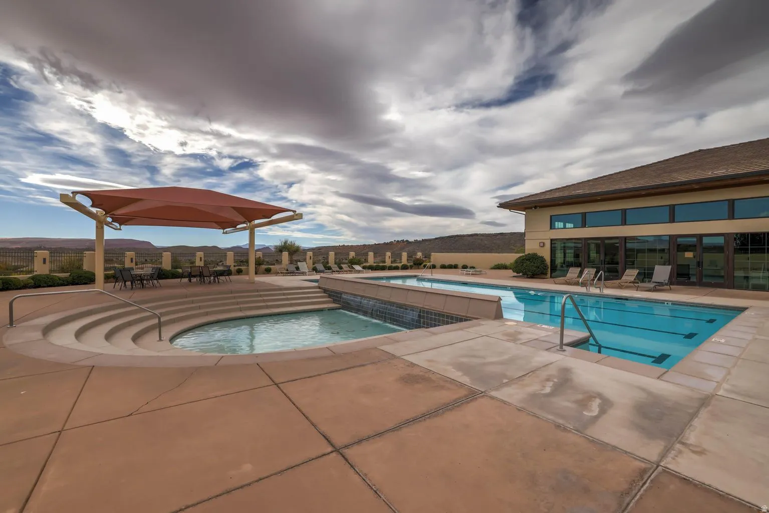 Swimming pool with integrated spa and water feature, expansive concrete decking, and an adjacent building with large windows