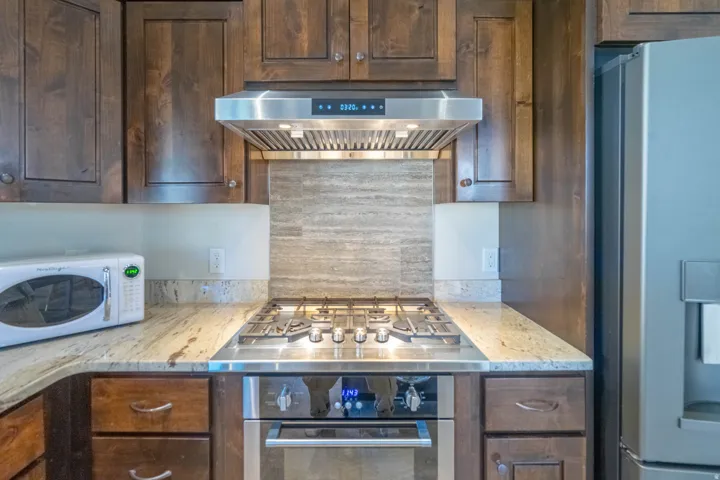 Stainless steel range hood, built-in oven, and gas cooktop complement rich wood cabinetry and stone countertops