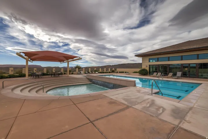 Swimming pool with integrated spa and water feature, expansive concrete decking, and an adjacent building with large windows