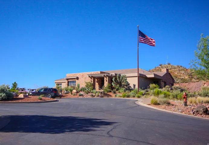 Paved drive with a desert landscape, a flag pole, and a stone-clad building