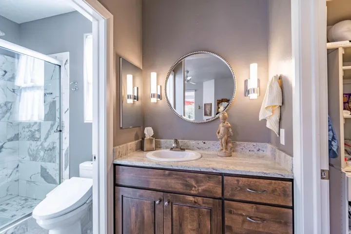 Granite-look countertop with an undermount sink, wood-finish vanity with cabinet storage, and a framed circular mirror