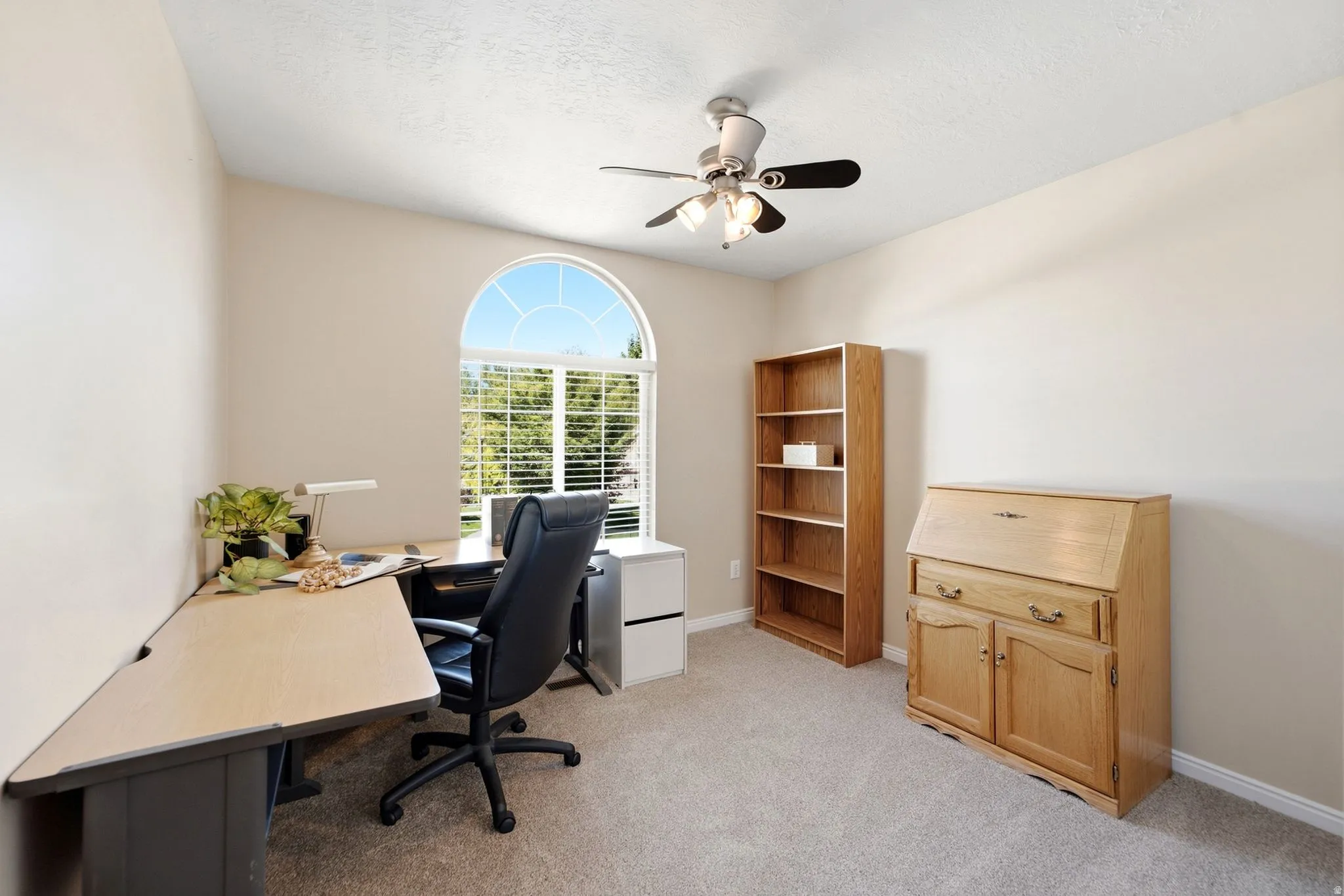 Arched window with gridded upper pane, carpet flooring, ceiling fan with integrated lighting, built-in shelving, and light-toned walls