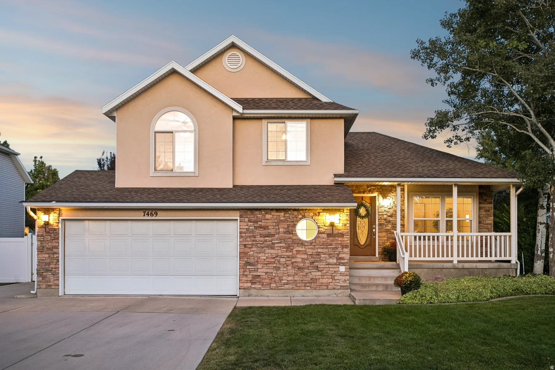 Stucco exterior with stone accent, two-car garage, covered porch, and arched windows